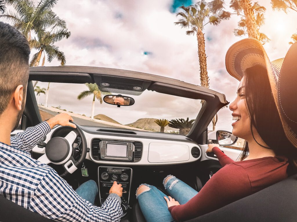 Happy young couple having fun during road trip in convertible car