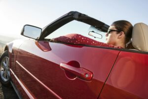 A young Caucasian woman in a convertible sports car.