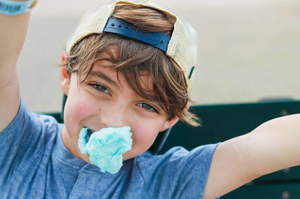 Boy with a cap enjoying blue cotton candy outdoors, smiling on a sunny day in Orlando, Florida